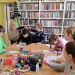na zdjęciu widać dzieci siedzące przy stole oraz bibliotekarkę w kapeluszu czarownicy
