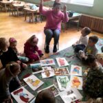 na zdjęciu widać dzieci siedzące na dywanie oraz bibliotekarkę okazujące im ilustracje przedstawiające misie z bajek