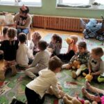 na zdjęciu widać dzieci siedzące na dywanie i słuchające czatającą im bibliotekarkę
