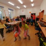 Dzieci zostały podzielone w pary i rozgrywają między sobą wyścigi z balonami trzymanymi w kolanach. Na pierwszym planie widać dwie rywalizujące ze sobą dziewczynki.