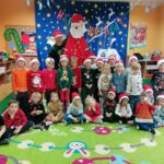 Uśmiechnięte przedszkolaki ustawiły się wszystkie razem do pamiątkowego zdjęcia. Razem z nimi stoi pan bibliotekarz, który dodatkowo trzyma w ręku wielką postać Mikołaja z czerwonego filcu.