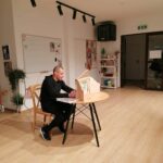 Pan bibliotekarz siedzi przy niewielkim okrągłym stoliku na którym ustawiony jest drewniany teatrzyk kamishibai i czyta przedstawienie pt. „Mój znajomy…” opowiadające o losach Nikifora.