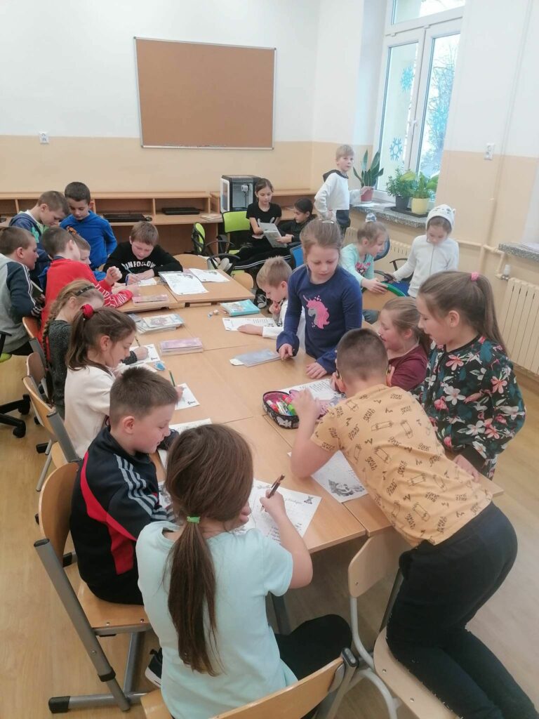 Wszyscy uczniowie siedzą przy złączonych stolikach i rozwiązują w skupieniu świąteczną krzyżówkę