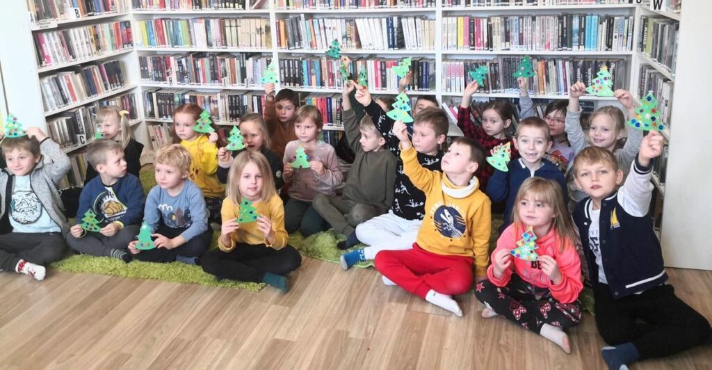 na zdjęciu widać dzieci siedzące na ziemi trzymające papierowe choinki