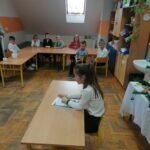 Uczniowie jednej z klas siedzą w ławkach pod oknami, natomiast na środku ich koleżanka czyta w skupieniu wylosowany tekst.