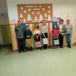 Na środku holu szkolnego mając za plecami gazetkę z zimowym napisem „Wesołych Świąt” stoją uśmiechnięci zwycięzcy konkursów, a w rękach trzymają swoje torby z nagrodami. Obok nich stoi Pani Dyrektor, Pani Bibliotekarka Szkolna oraz Pan Bibliotekarz z Filii w Bereście