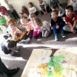 na zdjęciu widać dzieci siedzące na podłodze prze korową planszą