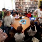 na zdjęciu widać dzieci siedzące wokół stołu w sali bibliotecznej.