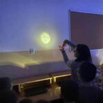 na zdjęciu widać salę szkolną, bibliotekarz wraz z dziećmi, rozszyfrowują symbole z ręcznie wykonanego projektora