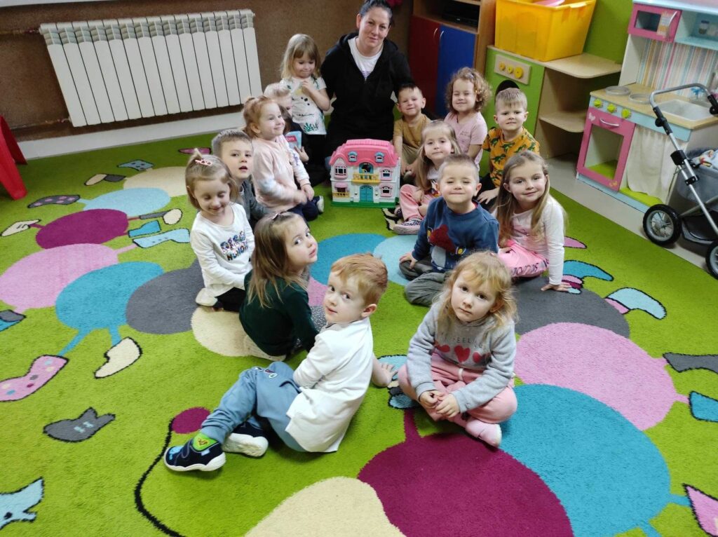 na zdjęciu widać salę przedszkolną, na dywanie siedzą dziecin i bibliotekarz