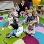 na zdjęciu widać salę przedszkolną, na dywanie siedzą dziecin i bibliotekarz