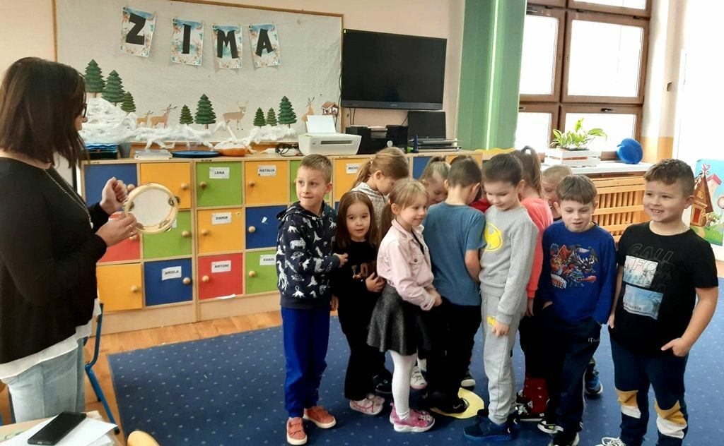 na zdjęciu widać stojącą kobietę oraz stojące przed nią dzieci