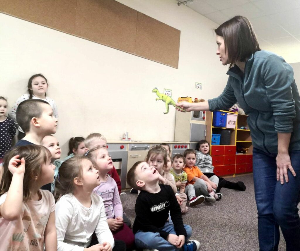 na zdjęciu widać bibliotekarkę pokazującą dzieciom dinozaura