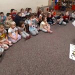 na zdjęciu widać bibliotekarkę czytającą dzieciom .Wszyscy siedzą na podłodze