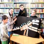 na zdjęciu widać dzieci trzymające prace przedstawiającą ogromnego dinozaura
