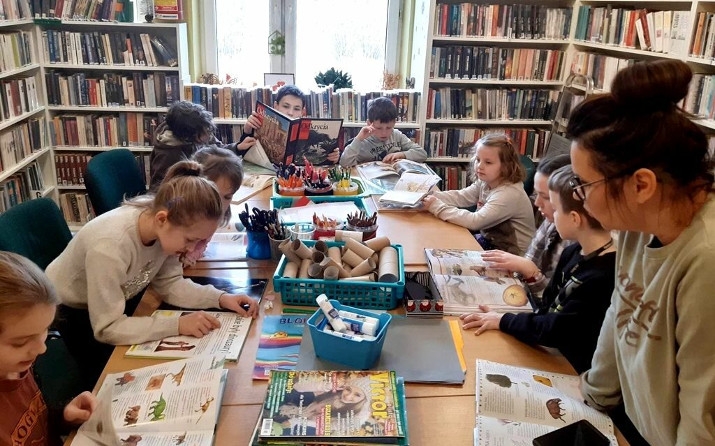 na zdjęciu widać salę biblioteczna oraz dzieci siedzące wokół stołu zapełnionego materiałami plastycznymi