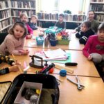 na zdjęciu widać salę biblioteczną, regały z książkami, okno i dzieci siedzące wokół stołu