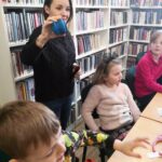 na zdjęciu widać bibliotekarkę pokazującą dzieciom niebieski przedmiot