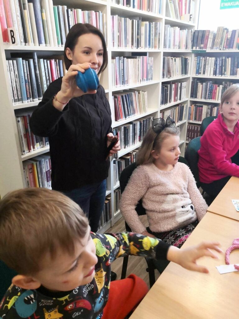na zdjęciu widać bibliotekarkę pokazującą dzieciom niebieski przedmiot
