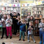 na zdjęciu widać dzieci stojące w sali bibliotecznej na tle regału z książkami
