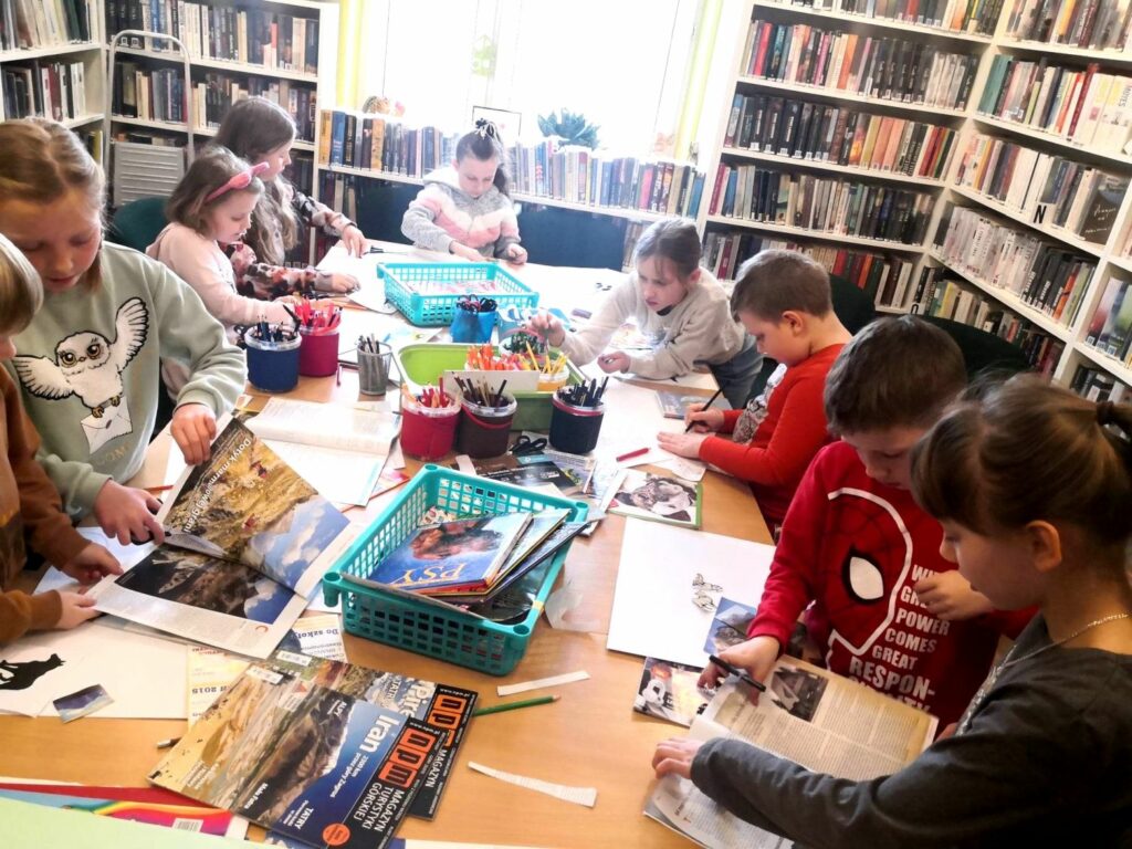 zdjęcie przedstawia salę biblioteczną oraz dzieci pracujące przy stole.