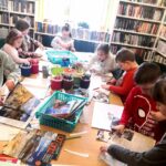 zdjęcie przedstawia salę biblioteczną oraz dzieci pracujące przy stole.