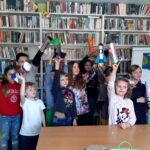 na zdjęciu widać dzieci stojące w sali bibliotecznej na tle regału z książkami