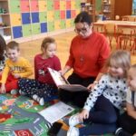 zdjęcie przedstawia bibliotekarkę czytająca dzieciom. Wszyscy siedzą na podłodze