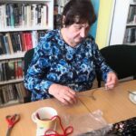 na zdjęciu widać Panią siedzącą przy stole i wykonującą prace plastyczne