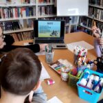 na zdjęciu widać dzieci siedzące przy stole patrzące w laptop w którym przedstawiony jest kot