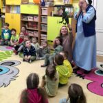 na zdjęciu widać sale przedszkolną, kolorowy dywan, dzieci oraz siostrę zakonną w niebieskim habicie