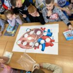 na zdjęciu widać stół, przy stole siedzą dzieci, układają puzzle