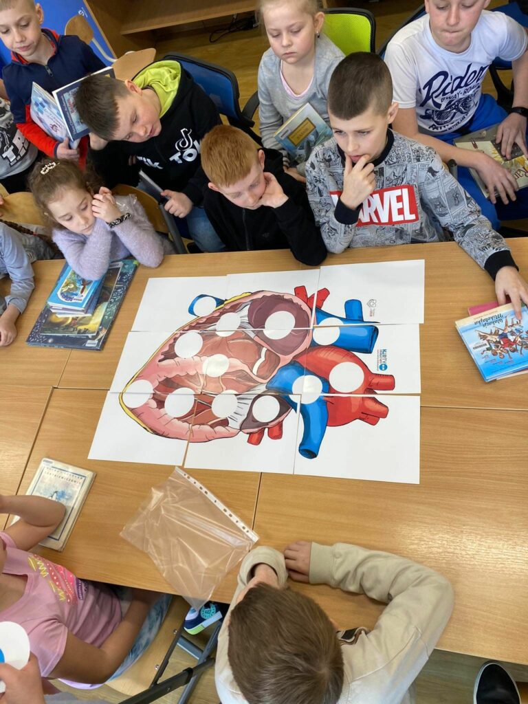 na zdjęciu widać stół, przy stole siedzą dzieci, układają puzzle