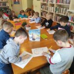 na zdjęciu widać salę biblioteczną, stół, wokół stołu siedzą dzieci, wykonują pracę plastyczną