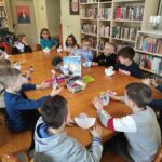 na zdjęciu widać salę biblioteczną, stół, wokół stołu siedzą dzieci, prezentują swoją pracę plastyczną