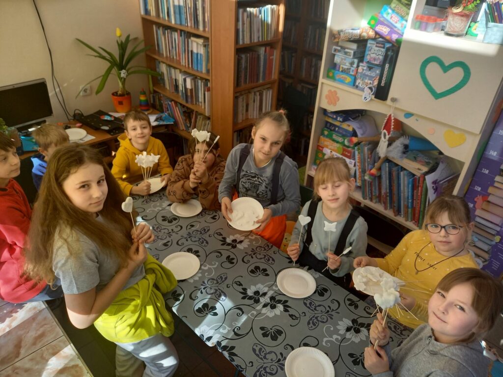 Grupa dzieci siedzi przy stole i prezentuje swoje prace