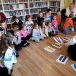 na zdjęciu widać dzieci oraz bibliotekarkę a na podłodze rozsypane kolorowe literki