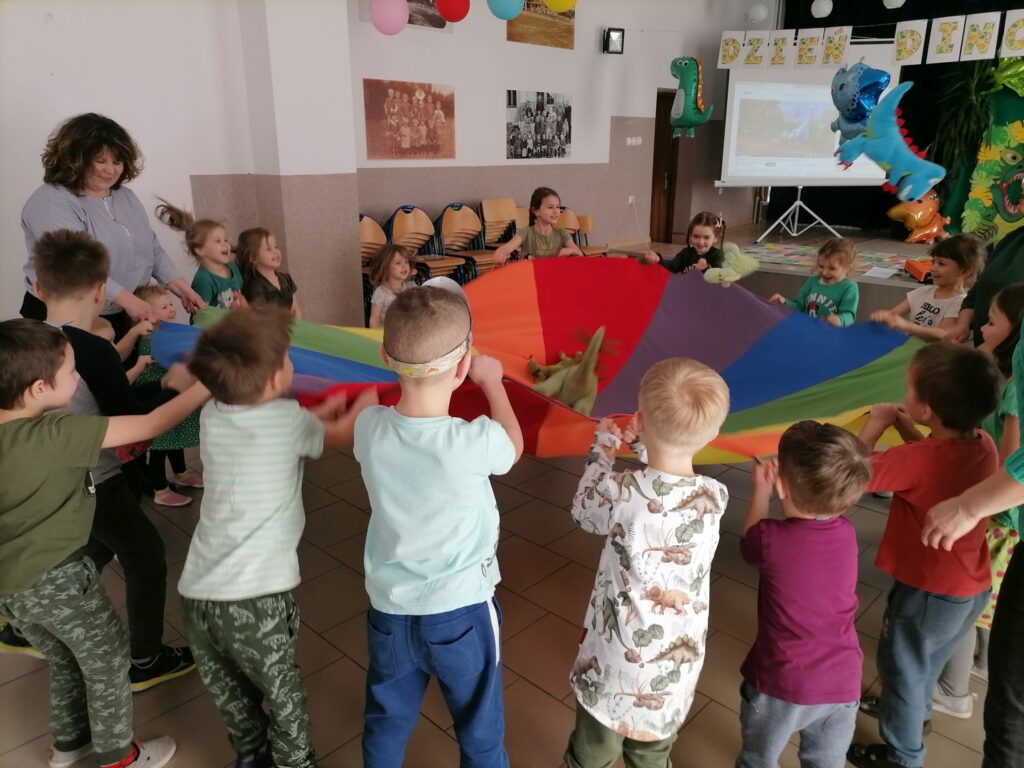 Na zdjęciu widoczna jest grupa przedszkolaków podczas zabawy chustą animacyjną.