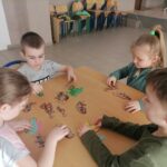 Na zdjęciu widocznych jest dwóch chłopców i dwie dziewczynki siedzących przy stoliku i dopasowujących szkielety dinozaurów do ich sylwetek.