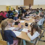 na zdjęciu widać salę szkolną, przy dużym stole siedzą dzieci, wykonują pracę plastyczną
