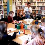 na zdjęciu widać dzieci siedzące wokół stołu w sali bibliotecznej
