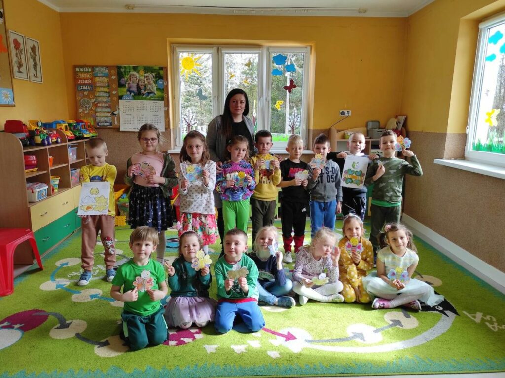 na zdjęciu widać salę przedszkolną, na środku sali stoją dzieci, prezentują wykonaną pracę plastyczną
