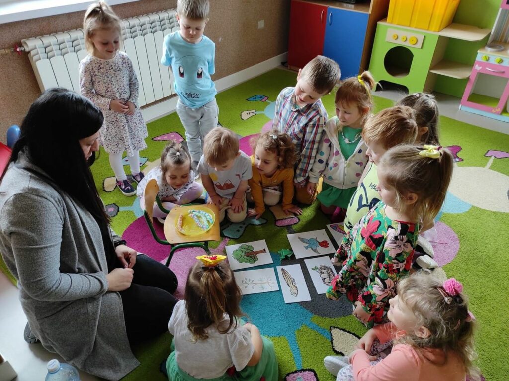 na zdjęciu widać dzieci z młodszej grupy przedszkolnej, obserwują eksperyment wykonany przez bibliotekarza