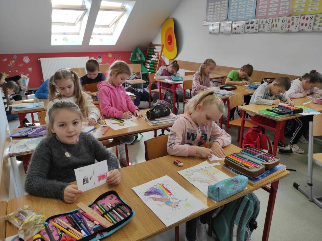 na zdjęciu widać salę szkolną, dzieci siedzą przy stolikach, rysują ilustracje