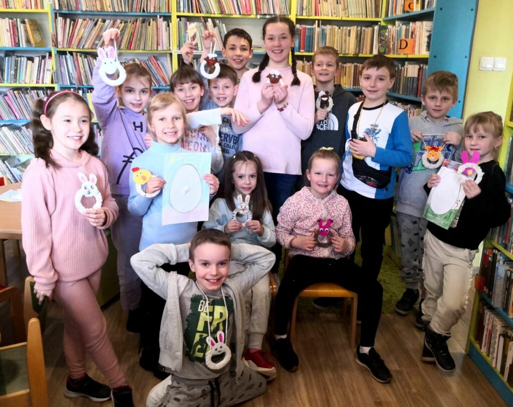 zdjęcie przedstawia dzieci stojące w sali bibliotecznej na tle regałów z książkami