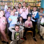 zdjęcie przedstawia dzieci stojące w sali bibliotecznej na tle regałów z książkami