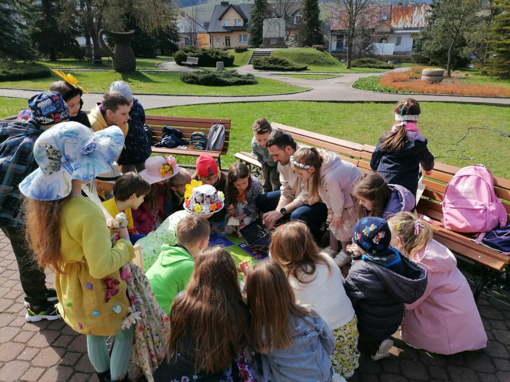 Na zdjęciu widoczna jest grupa dzieci obserwująca pokaz umiejętności edukacyjnego robota Photona prezentowanego przez pracownika biblioteki.