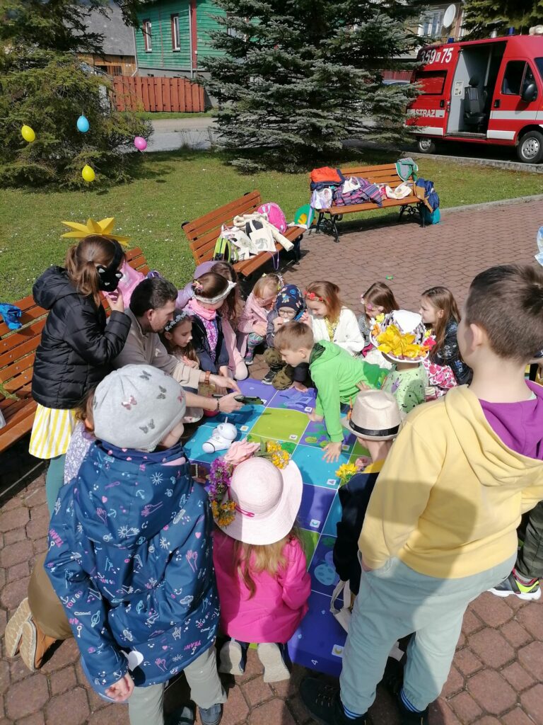 Na zdjęciu widoczna jest grupa dzieci obserwująca pokaz umiejętności edukacyjnego robota Photona prezentowanego przez pracownika biblioteki.