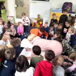 na zdjęciu widać dzieci w wieku przedszkolnym siedzące na podłodze wokół kolorowych ilustracji