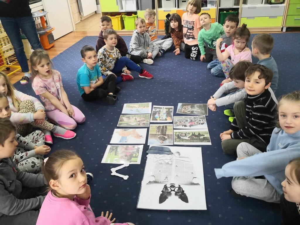 na zdjęciu widać dzieci w wieku przedszkolnym siedzące na niebieskim dywanie
